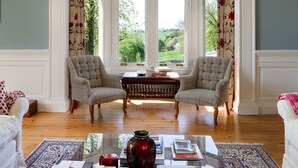 A room with two armchairs facing a large window, a coffee table with books and a vase, and a patterned rug. - Balmule House (Dunfermline)