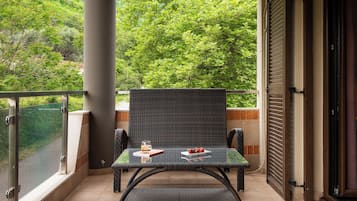 A balcony with a wicker chair and table, a glass door, and a view of lush greenery.