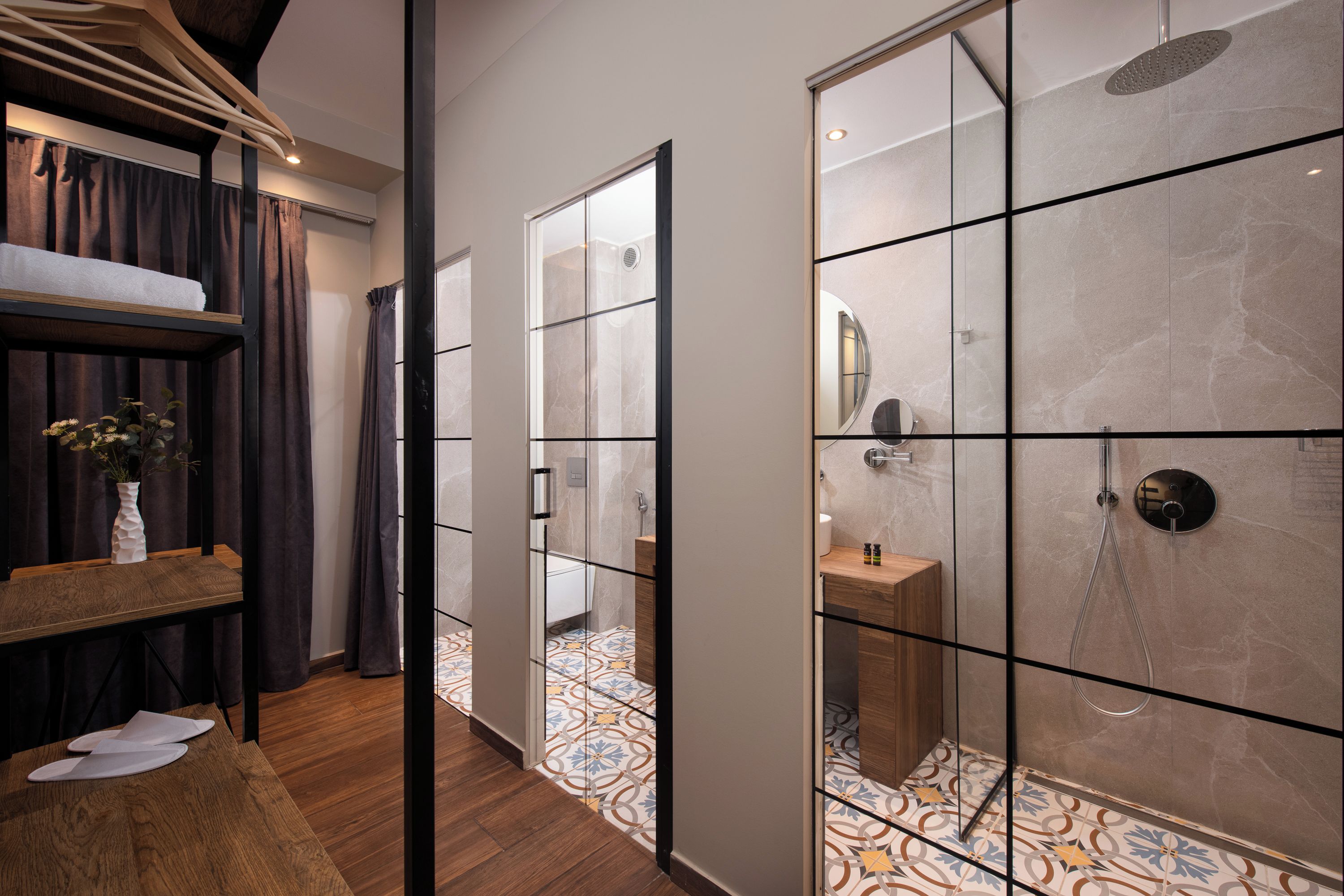 A modern bathroom with a shower, a sink, and a mirror. There is a patterned floor and a wooden bench.