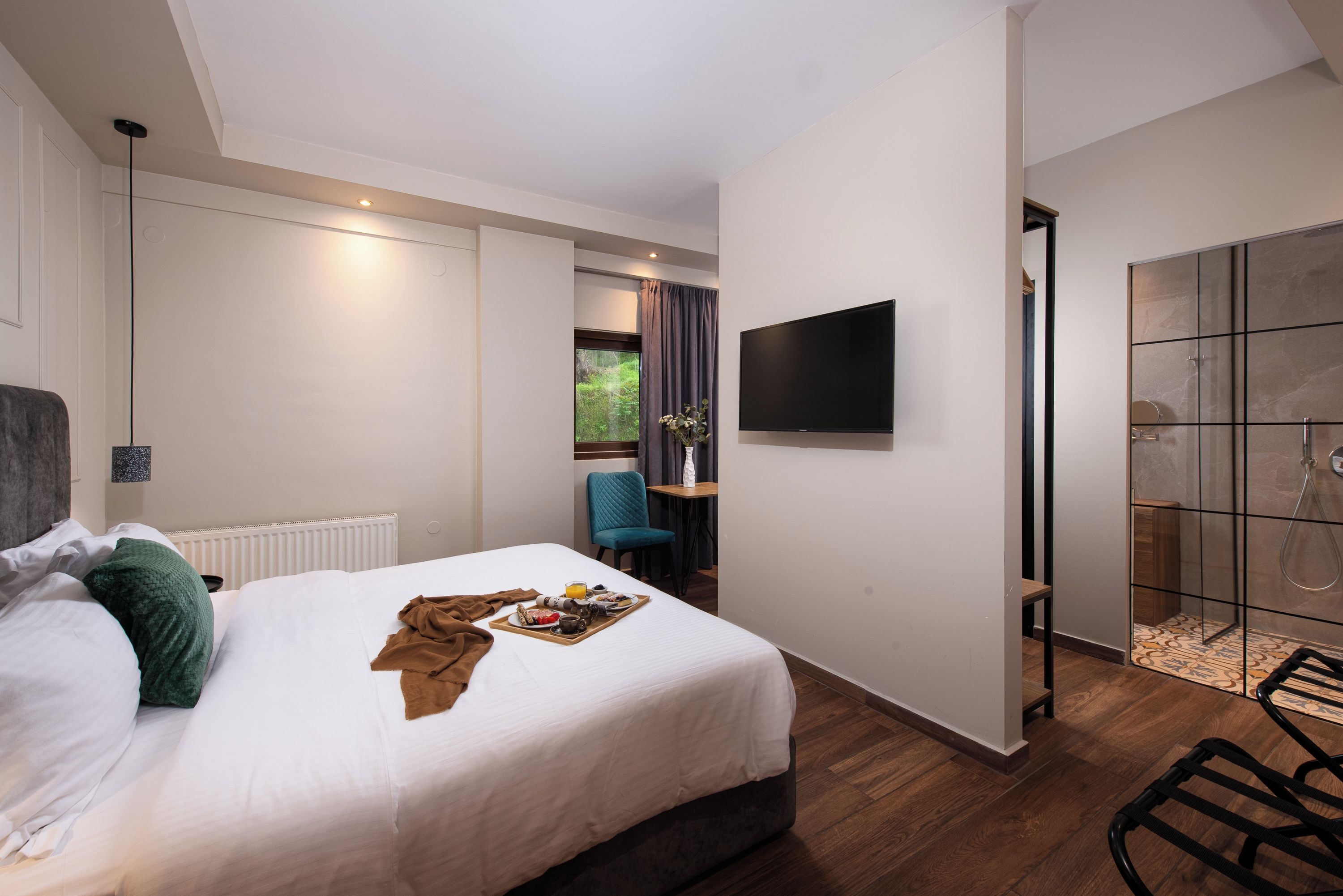 Habitación de hotel con cama, televisor de pantalla plana, una mesita con silla y zona de ducha.