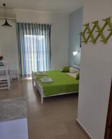 A bedroom with a bed, a desk, and a chair. There is a window with curtains and a wall-mounted light fixture.