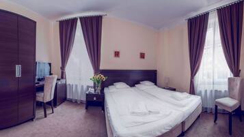 Een hotelkamer met een groot bed, een bureau, een stoel, een kledingkast en twee ramen met gordijnen.