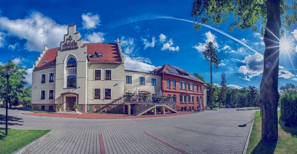 A historic building with a red roof, a central staircase, and a paved courtyard. - Hotel Niemcza SPA (Niemcza)