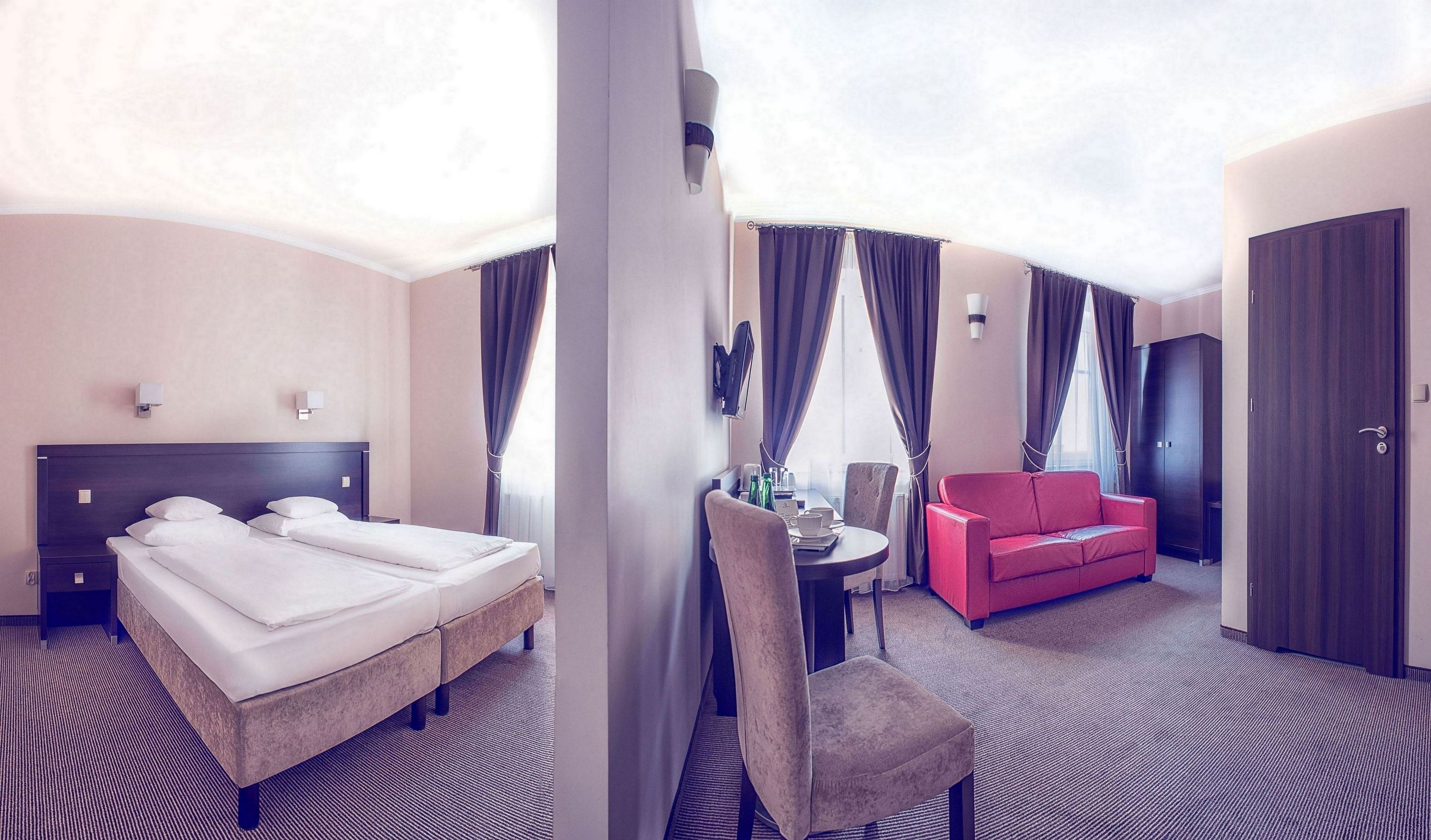A hotel room with a bed, a red sofa, a desk with a chair, and a wardrobe.