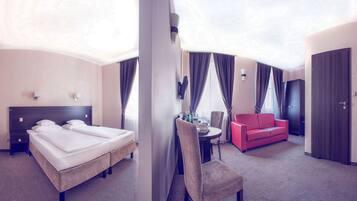 A hotel room with a bed, a red sofa, a desk with a chair, and a wardrobe.