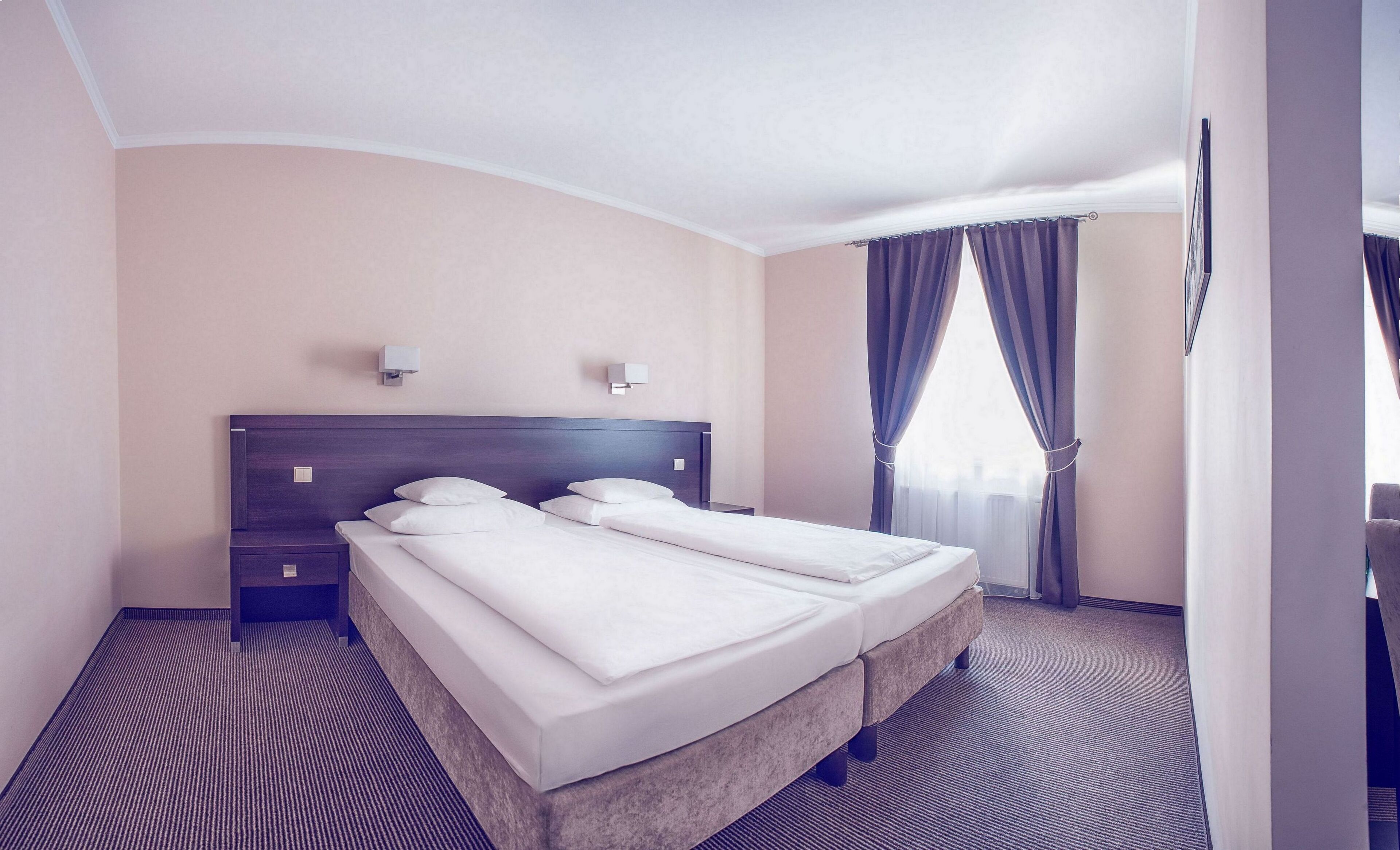 Habitación de hotel con una cama grande, dos mesitas de noche, un cabecero y una ventana con cortinas.