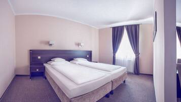 Habitación de hotel con una cama grande, dos mesitas de noche, un cabecero y una ventana con cortinas.