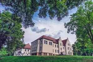 A large, multi-story building with a red-tiled roof, surrounded by lush greenery and trees. - Hotel Niemcza SPA (Niemcza)
