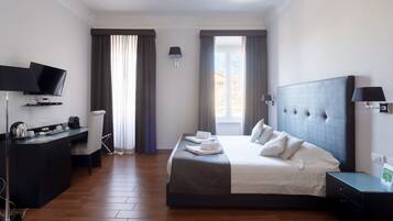 Habitación de hotel con cama, escritorio, televisión y ventana con cortinas.