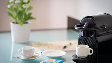 A coffee machine, two cups, a plate, and a packet of coffee on a table.
