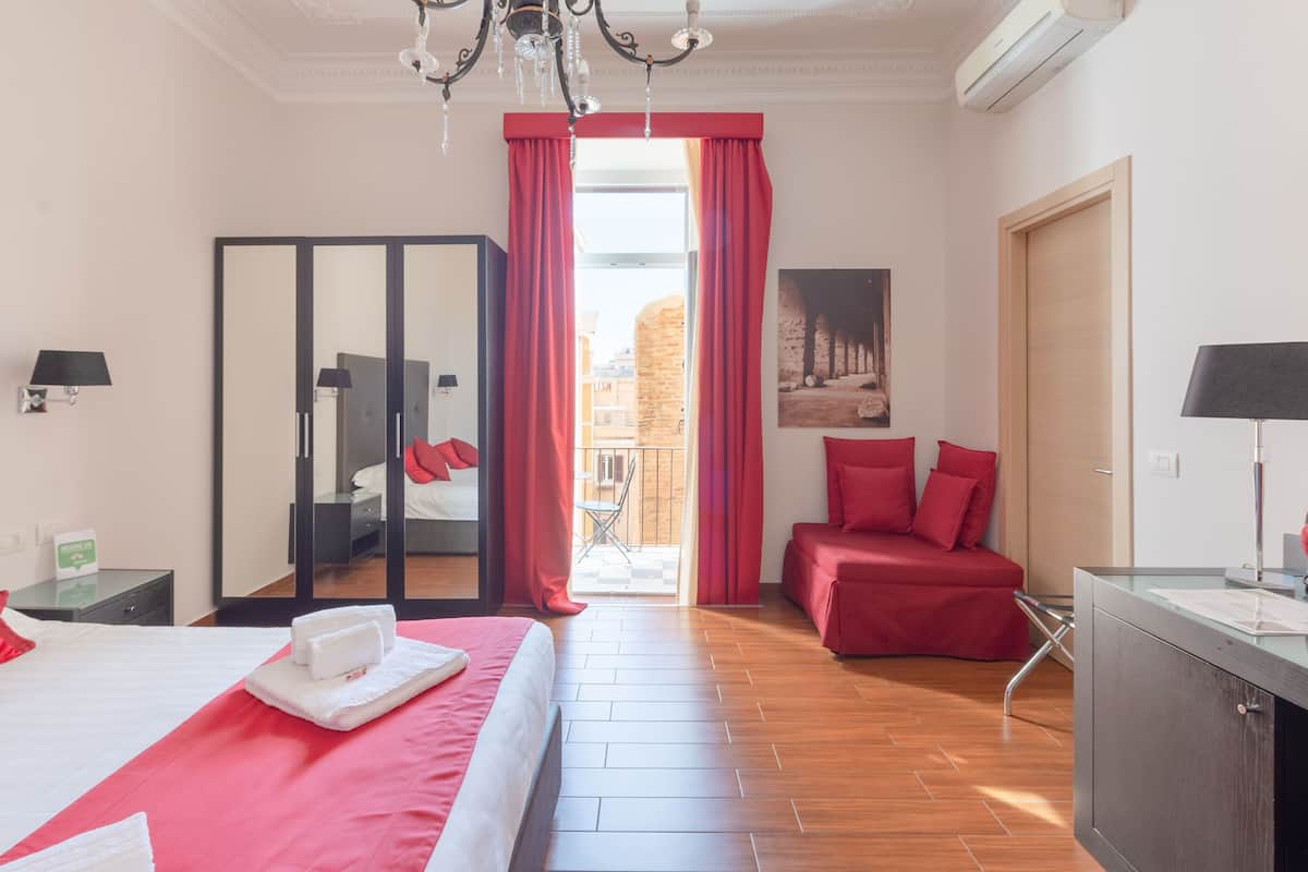 A hotel room with a bed, a desk, a chair, a wardrobe, and a balcony with red curtains.