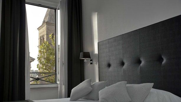 Una habitación de hotel moderna con una cama grande, cabecera y vista a un edificio a través de una ventana.