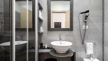 Un baño moderno con cabina de ducha de vidrio, un lavabo blanco con un espejo encima y un secador de pelo fijado en la pared.