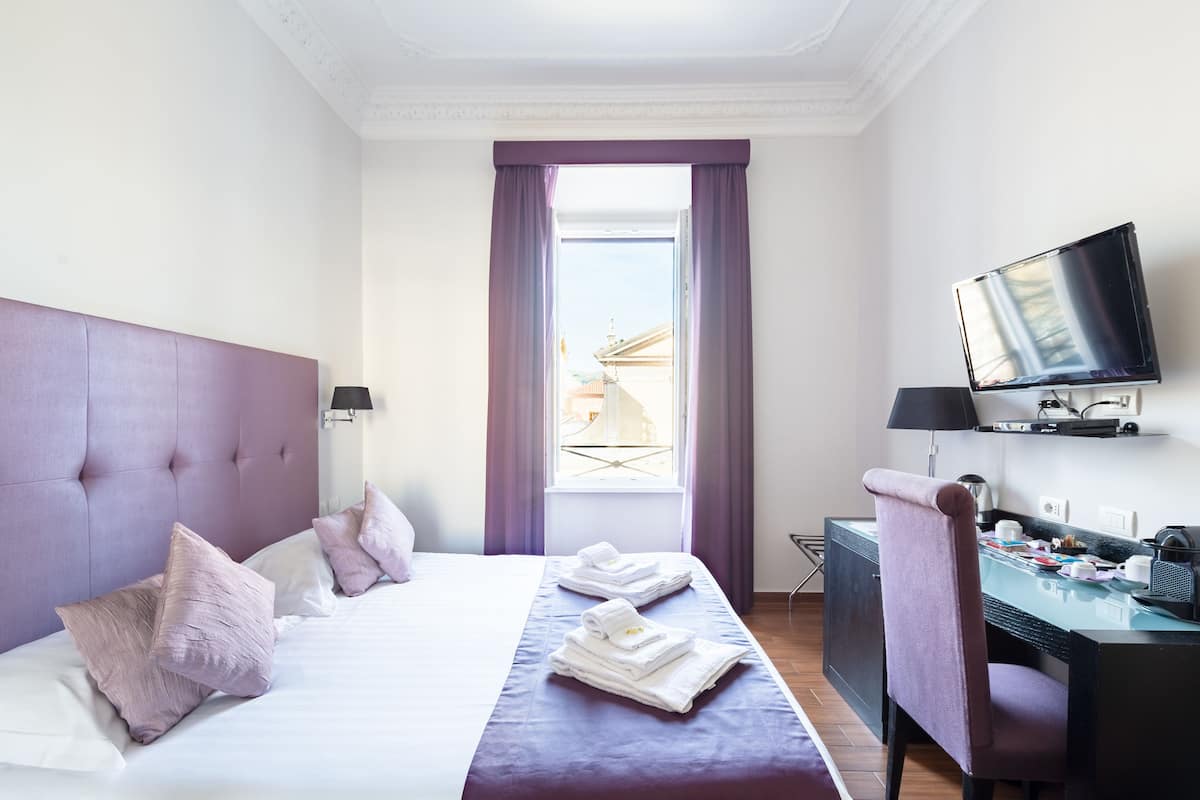 A hotel room with a large bed, a desk with a chair, a television, and a window with curtains.