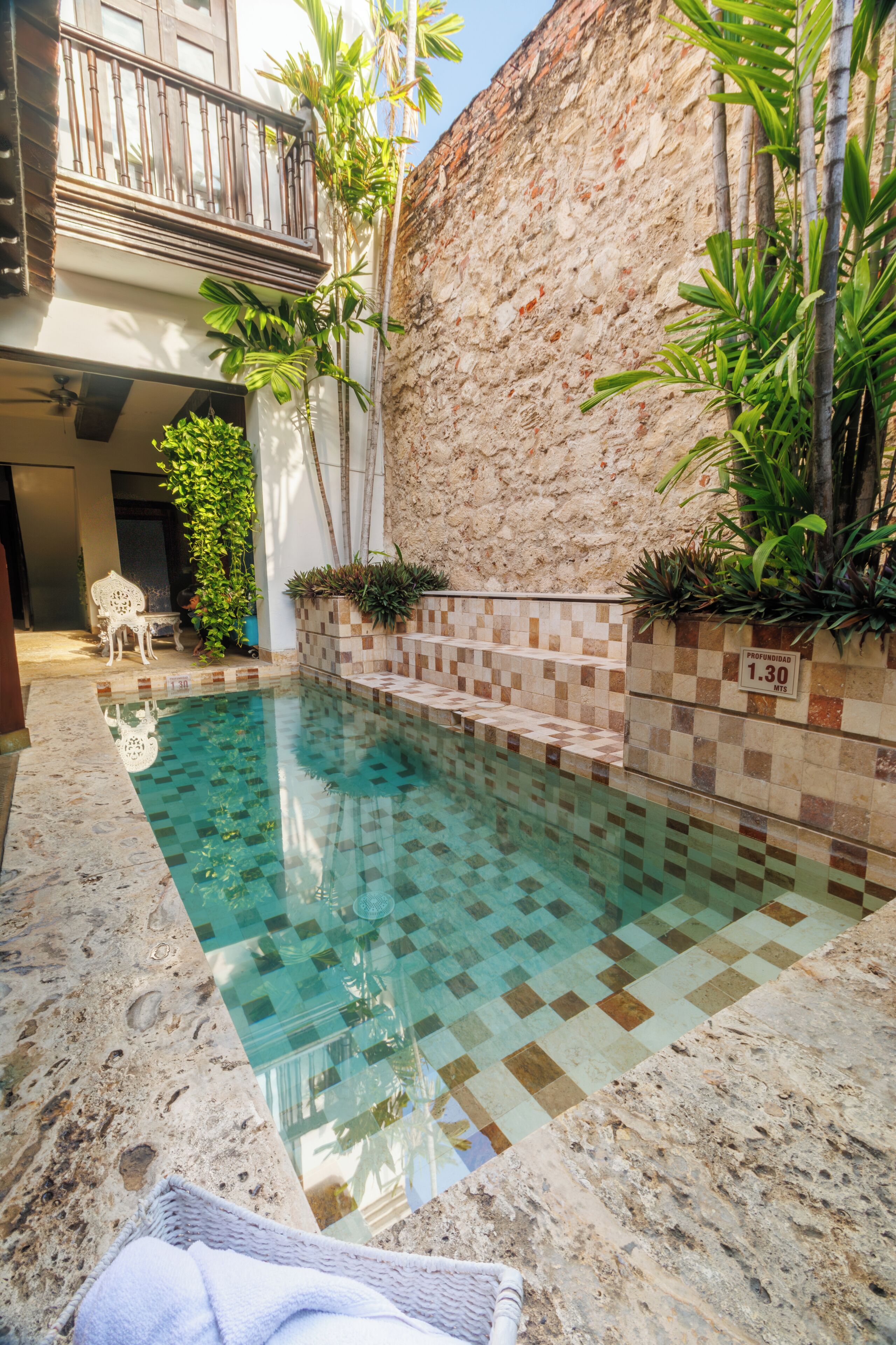 Una piscina con suelo de baldosas, pared de piedra y una silla.