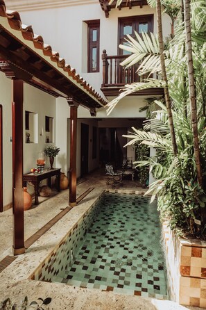 Une cour avec une piscine carrelée, une pergola en bois et des plantes en pot.