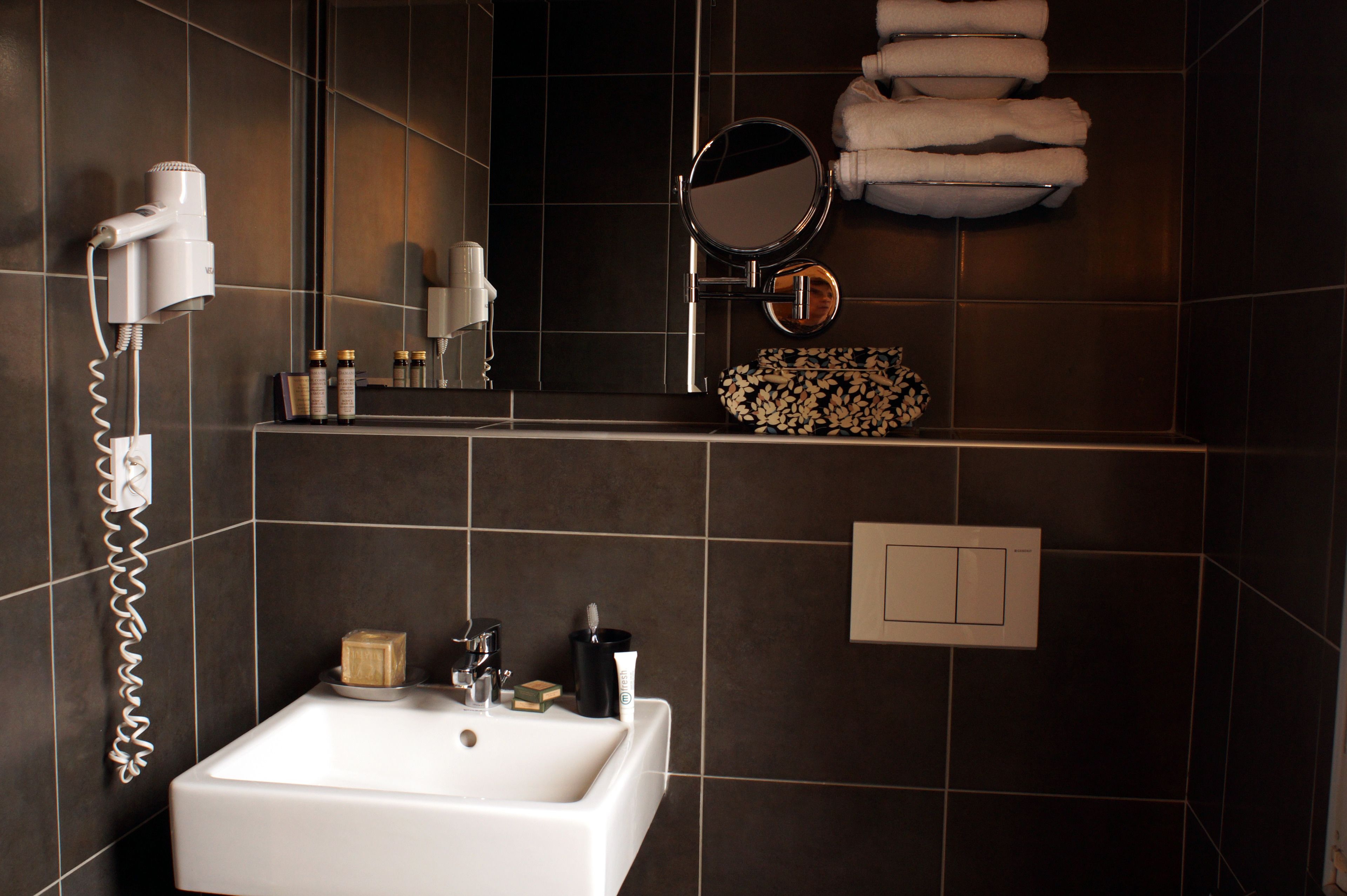 Une salle de bain avec un lavabo blanc, un sèche-cheveux, un miroir et une étagère contenant des articles de toilette.