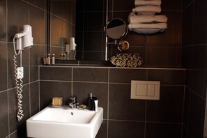 A bathroom with a white sink, a hairdryer, a mirror, and a shelf with toiletries.