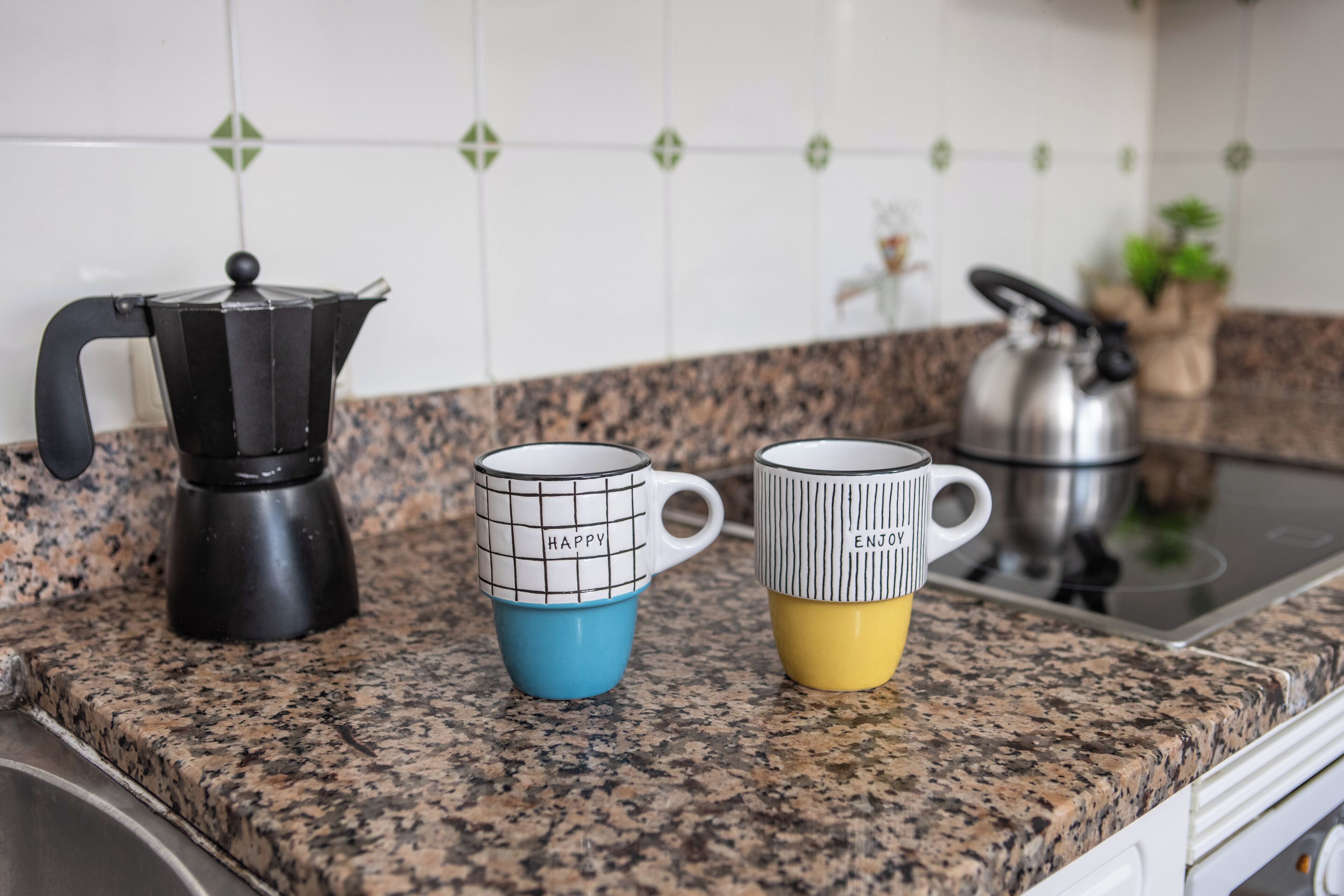 Een keukenblad met een koffiezetapparaat, twee mokken en een waterkoker.