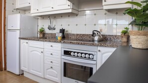 A kitchen with white cabinets, a granite countertop, a built-in oven, and a refrigerator. - RVApartaments La Pineda (Torroella de Montgrí)