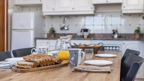 A breakfast table set with bread, a mug, a glass, and a pitcher of orange juice in a kitchen with white cabinets and a tiled backsplash. - RVApartaments La Pineda (Torroella de Montgrí)