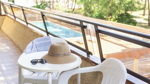 A balcony with a pool view, a white plastic chair, a small round table with a straw hat and sunglasses on it. - RVApartaments La Pineda (Torroella de Montgrí)
