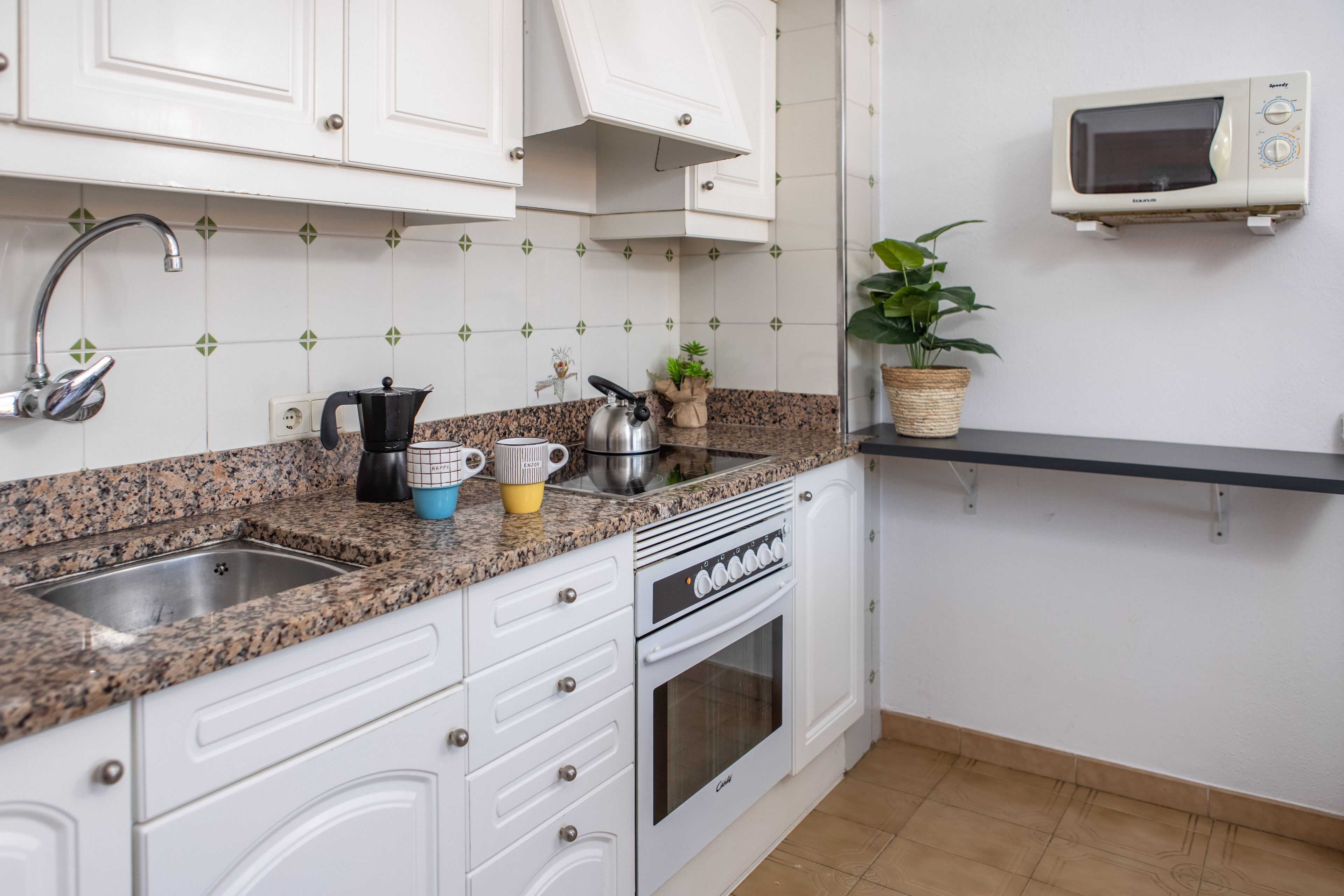 A kitchen with white cabinets, granite countertops, a built-in oven, a microwave, and a potted plant.