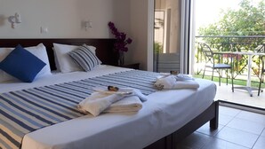 Een hotelkamer met een groot bed, een balkon met een tafel en stoelen, en een schuifdeur die naar het balkon leidt.