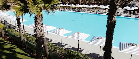 Ein Poolbereich mit Liegestühlen und Sonnenschirmen, umgeben von Palmen.