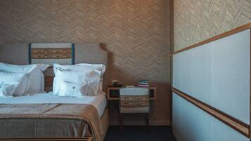 Ein Hotelzimmer mit Bett, Sessel, Nachttisch und Wand mit Fischgrätmuster.