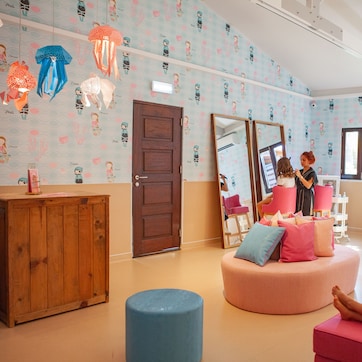 A room with a wooden cabinet, a round seating area with cushions, a large mirror, and a massage table.