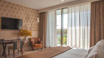 A hotel room with a bed, a desk with a chair, a TV mounted on the wall, and a large window with curtains.