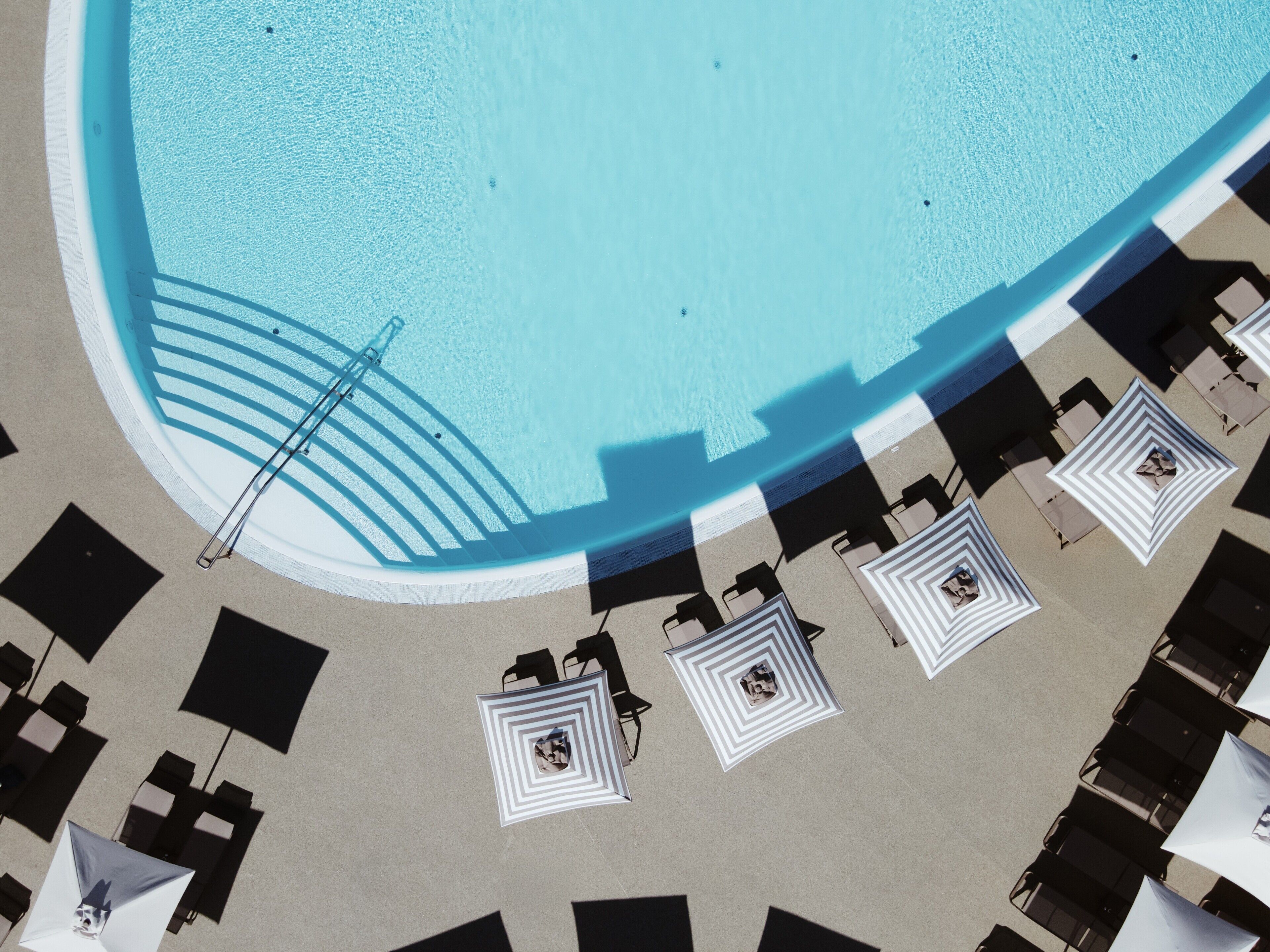 Vue aérienne d’une piscine dotée d’un espace ombragé et de chaises longues.