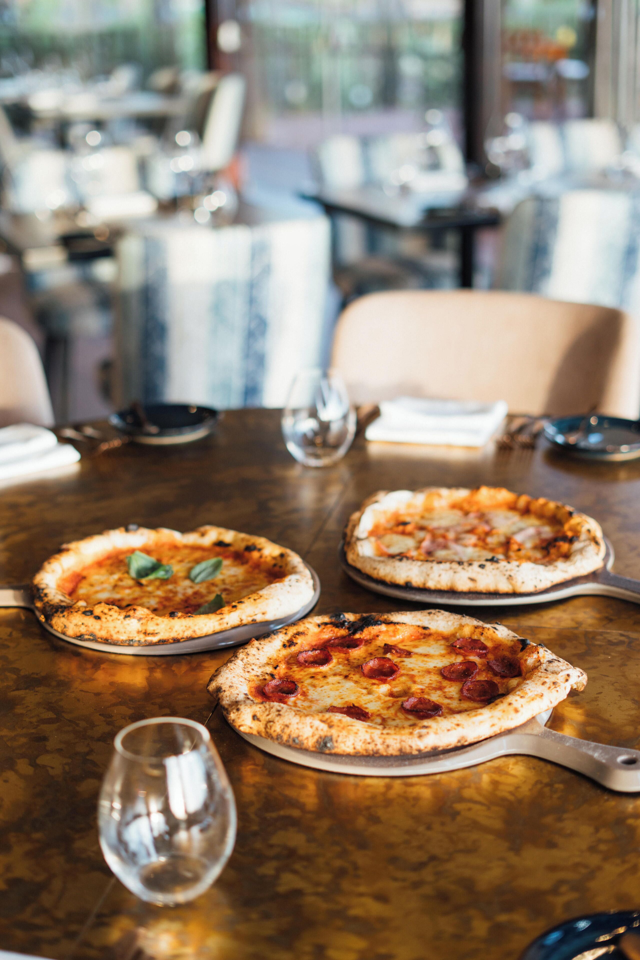A restaurant table with three pizzas and a wine glass.