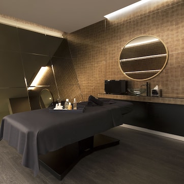 A modern spa room with a massage table, a large mirror, and a round mirror on the wall.