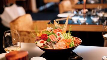 A bowl of assorted seafood and vegetables on a table with a wine glass and chopsticks.