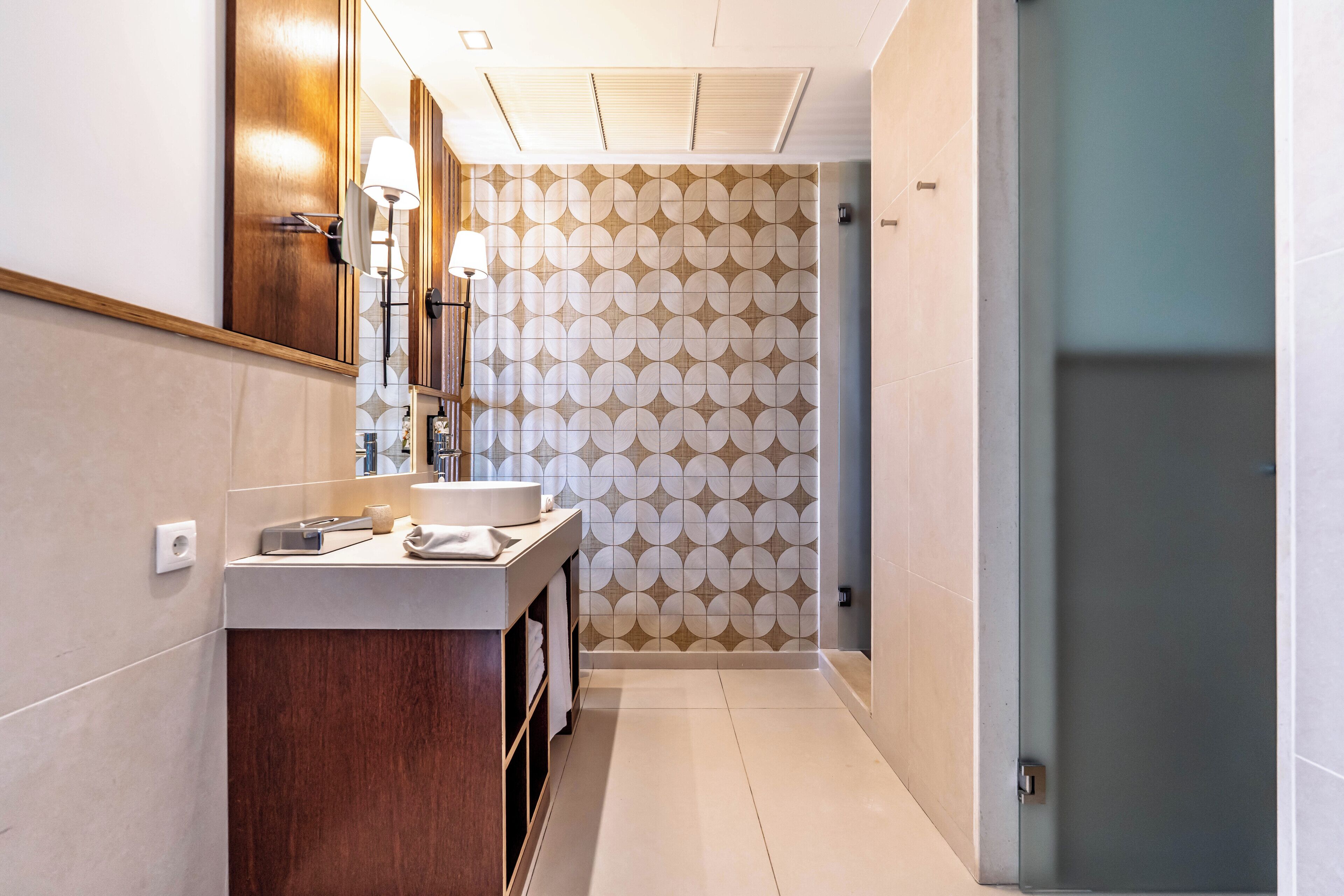 Une salle de bain moderne avec un meuble-lavabo en bois, un miroir, un porte-serviettes et un mur décoré d’un motif.
