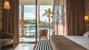 A hotel room with a bed, a chair, a table, and a view of palm trees and a pool. - Wine & Books by the sea (Albufeira)
