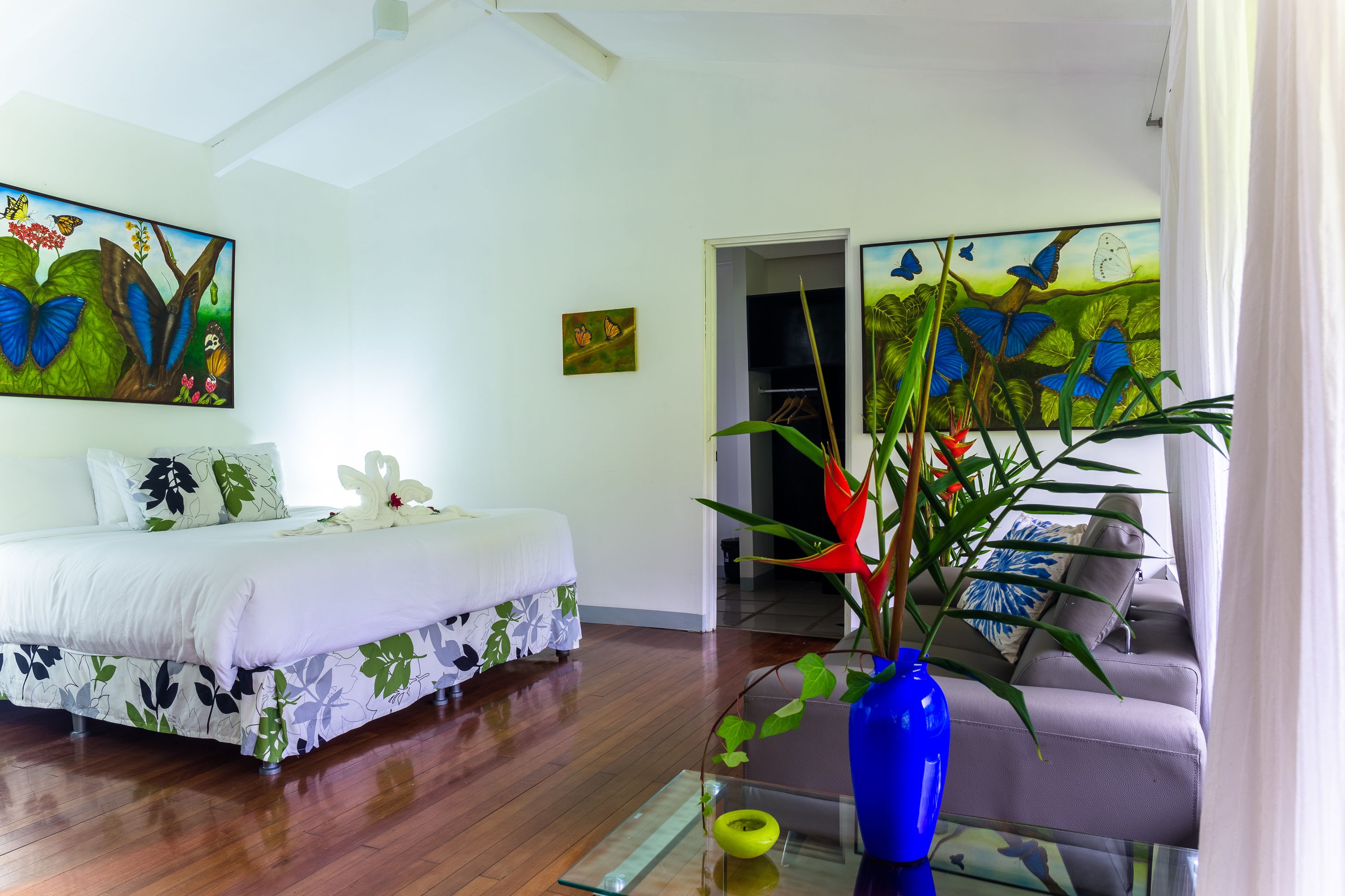 A bedroom with a bed, a sofa, a glass coffee table, and a vase with flowers.