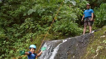A person rappelling down a rocky waterfall in a forested area.