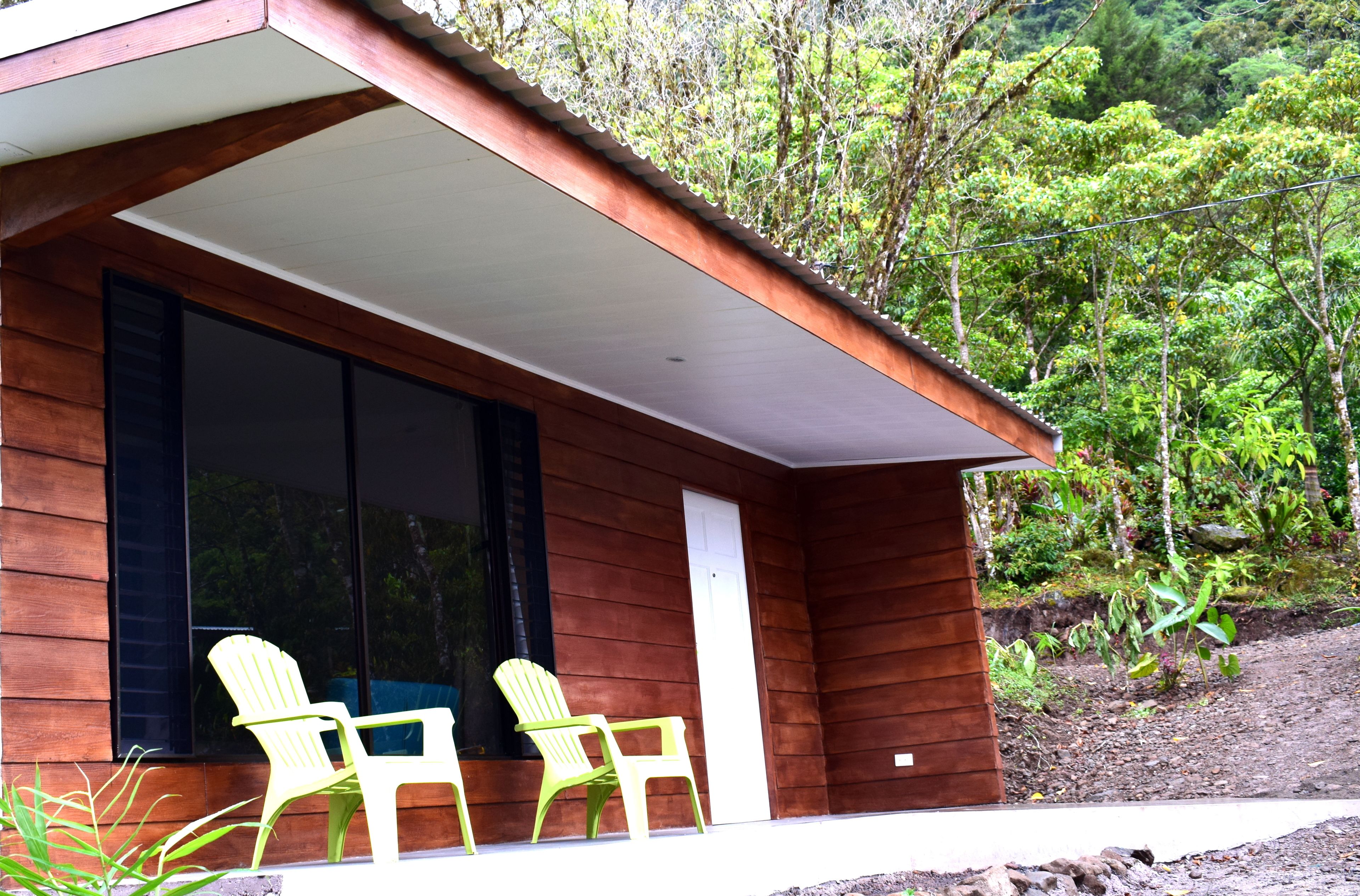 A wooden house with a covered porch and two green chairs outside.