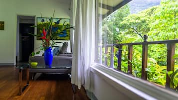 A living room with a glass coffee table, a sofa, and a large window with a view of lush greenery.
