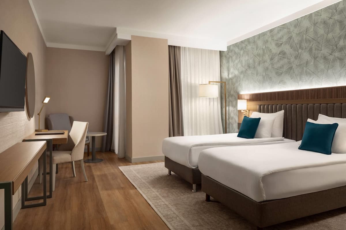 Habitació d'hotel amb dos llits, una taula de nit, una cadira, un televisor i un mur amb un disseny decoratiu.