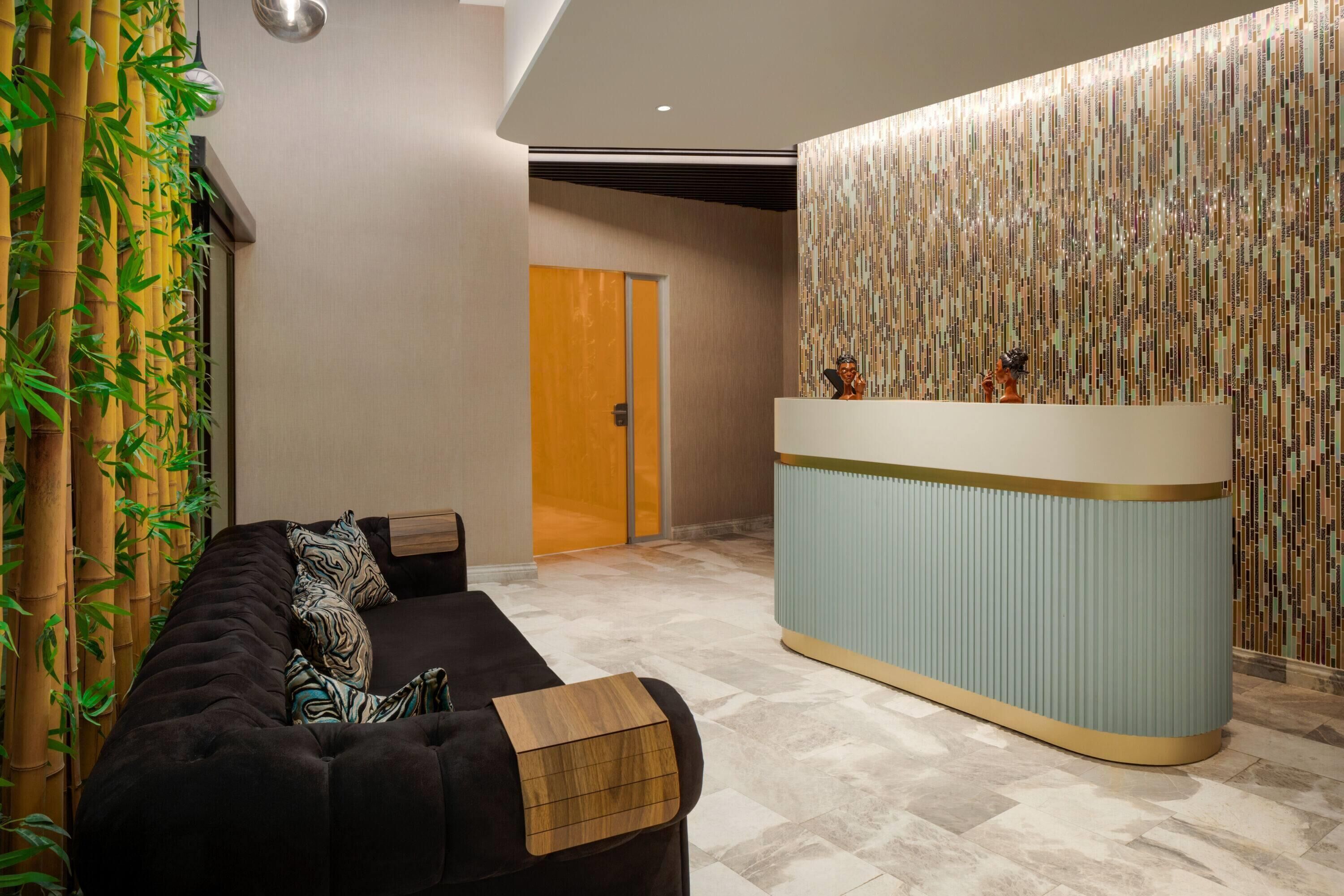 A reception area with a reception desk, a black sofa with patterned cushions, and a wall with vertical bamboo-like panels.