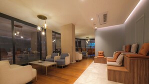 A modern lounge area with seating arrangements, a marble floor, and a view of the cityscape through large windows. - Ramada Encore by Wyndham Konya Karatay (Konya)