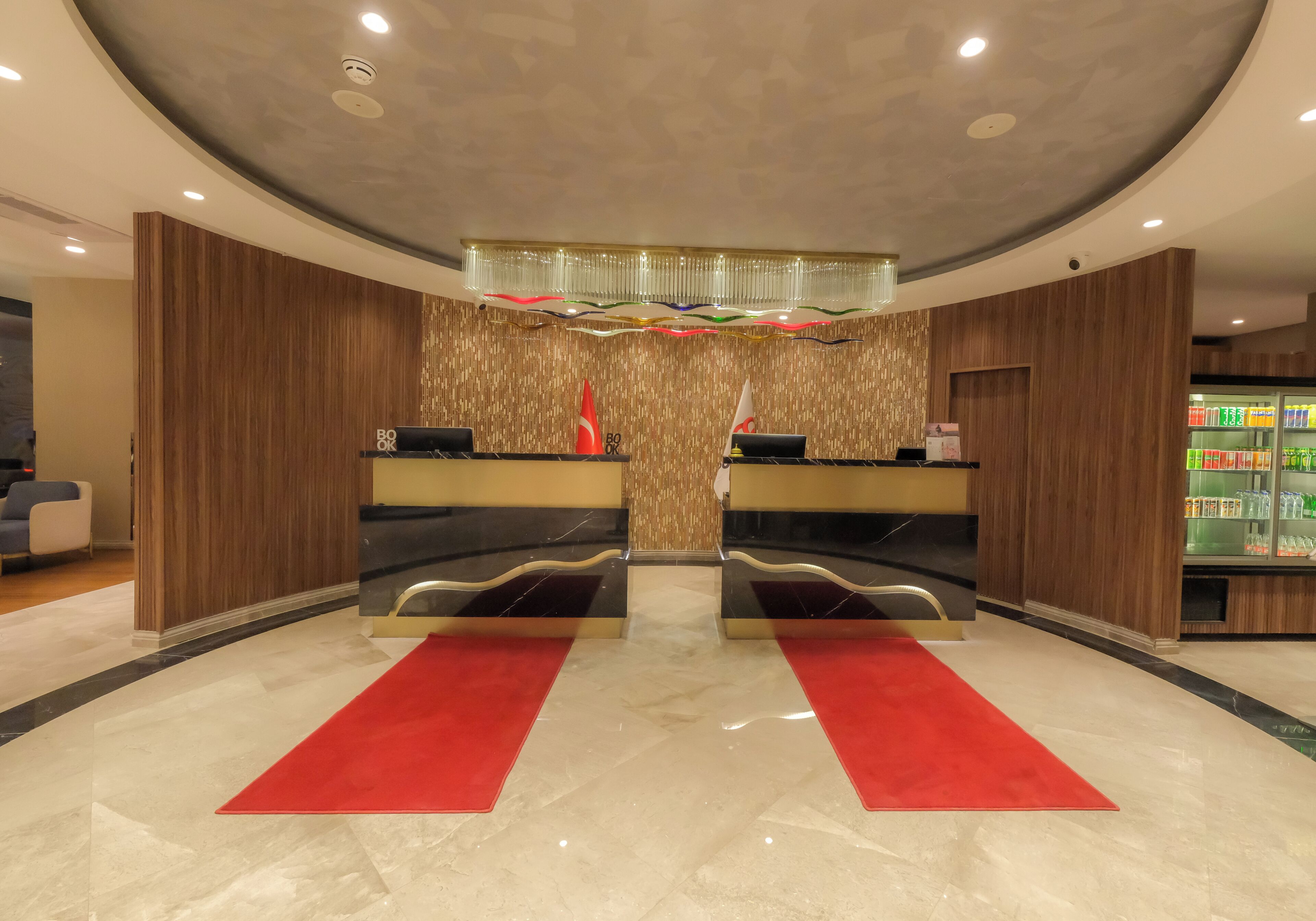 A hotel reception area with a modern design, featuring a reception desk, a chandelier, and a red carpet.