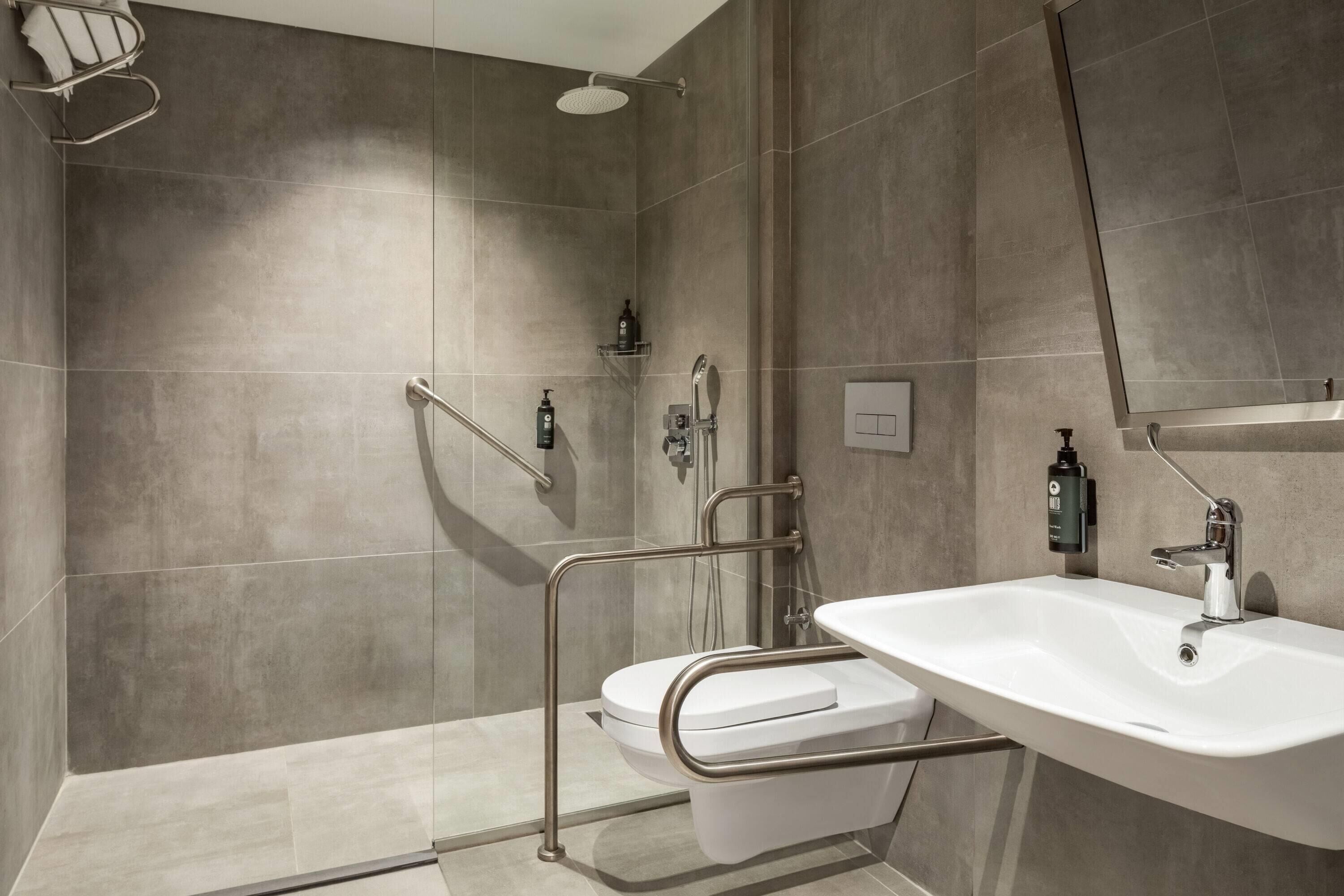 A modern bathroom with a shower, toilet, and sink, equipped with grab bars and a handheld showerhead.