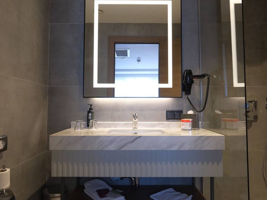 Een moderne badkamer met een grote spiegel, een wastafel, een haardroger en een douche.