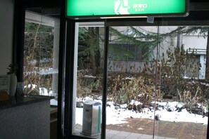Una puerta de cristal con un letrero de salida verde, una máquina expendedora y vistas a un área exterior nevada con árboles.