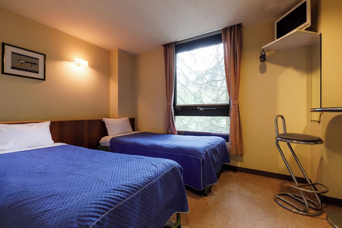 Habitació d'hotel amb dos llits, un televisor, una finestra amb cortines i una taula petita.